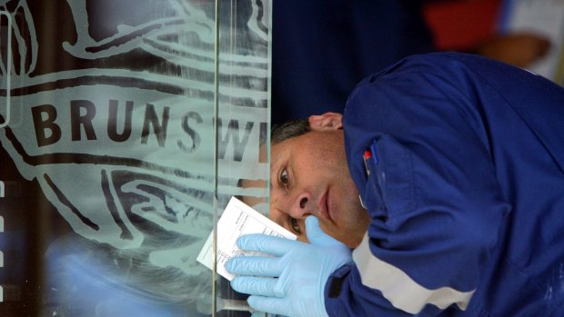 A member of Police Forensics looks for fingerprints on the glass front doors of the Brunswick Club where Lewis Moran was shot and killed in 2004.
