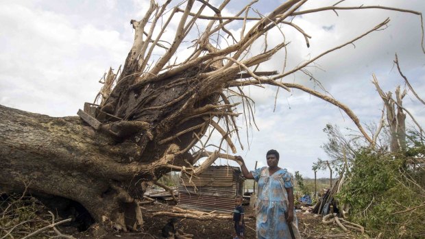 A woman and her child stand next to a large tree that nearly fell on their home in Port Vila.