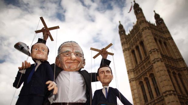 A man in a Rupert Murdoch mask holds puppets depicting British Prime Minister David Cameron (left) and Culture Secretary Jeremy Hunt outside Parliament.