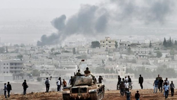 Turkish soldiers on a tank and Kurdish people look at the Syrian town of Kobane.