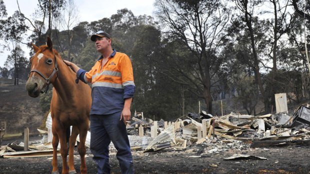 Anthony Sexton with his horse, which is burnt,  stands before the smouldering ruins of his home at Koornalla near Churchill, in South Gippsland.