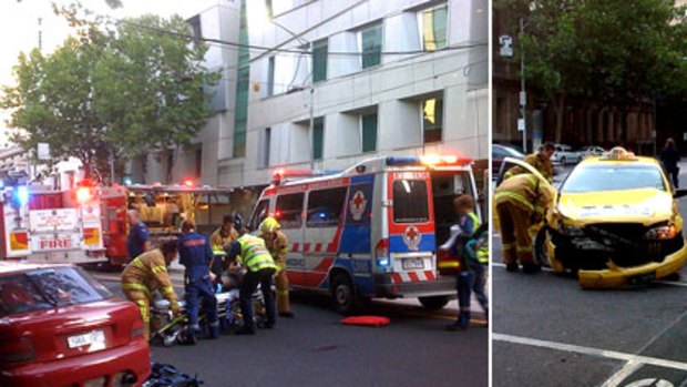 A man injured in the crash is treated on William Street, while firefighters inspect the damaged taxi.