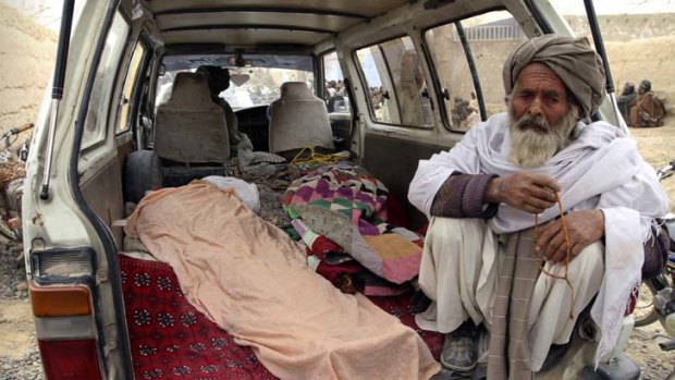 Adding to the toll ... an Afghan man sits by the covered body of one of the victims of the massacre in Kandahar province.