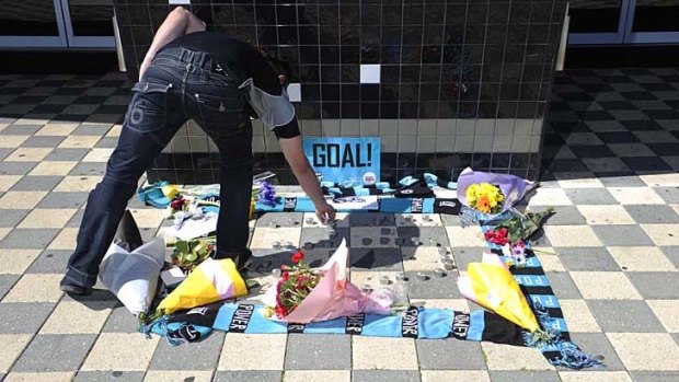 Port fan Vince Esposito places a candle at a makeshift shrine to John McCarthy outside the club's Adelaide headquarters.