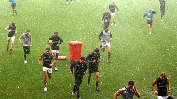 Essendon players run for cover as rain falls during training at Windy Hill yesterday.