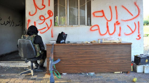 A gunman who said he was with the 'Taliban Council' sits at the Bab al-Hawa border post. The graffiti reads ''there is no god but God'' and ''Islam is the solution''.