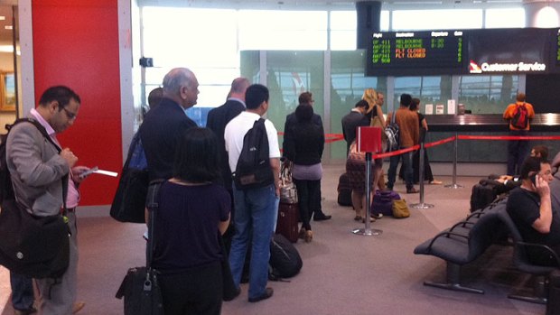 Passengers queue at a crowded service desk where Qantas staff were issuing handwritten boarding passes after a computer meltdown this morning.