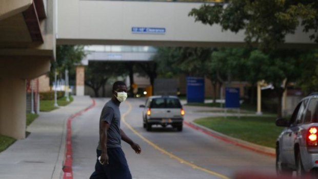 A pedestrian wears a surgical mask as he crosses the street in front of Texas Health Presbyterian Hospital, where Thomas Eric Duncan is being treated.  