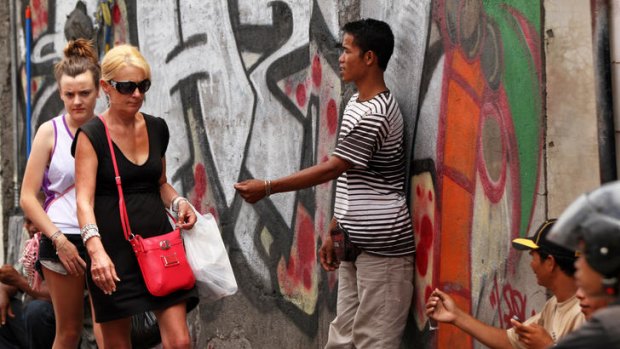 Tourists in Bali walk past a street seller only metres from where a 14-year-old NSW schoolboy was arrested.