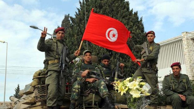Tunisian soldiers holding a Tunisian flag stand guard in their tank in Carthage.
