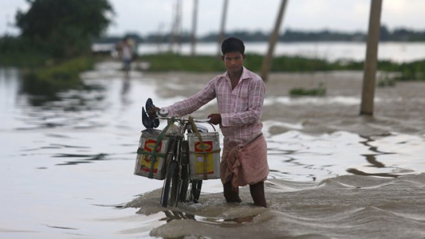 Floods displace thousands: A man pushes his bicycle past a flooded road in Ashigarh village, about 70 kilometers east of Gauhati, India.