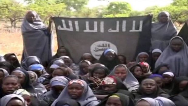 An image of the kidnapped girls wearing the full-length hijab and holding a flag saying, ''There is no god, but Allah''.