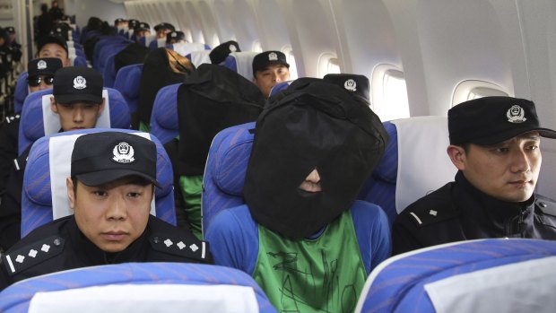 Chinese suspects involved in wire fraud, centre, sit in a plane as they arrive at Beijing Airport on Wednesday.
