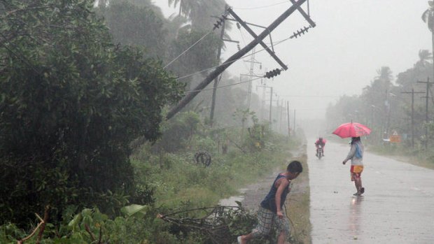 Residents brave heavy rain near a tilted power pole.