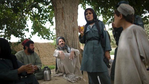 An Afghan policewoman drinks tea with local villagers. Women are moving up the ranks in the police force.