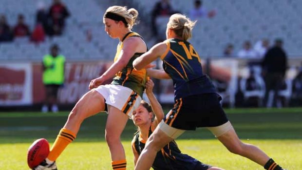 Lauren Arnell gets a kick away as Kiara Bowers and Monica O'Brien (No. 14) try for the tackle at the MCG in the Green All Stars versus Brilliant Gold from the AFL women's high performance academy.