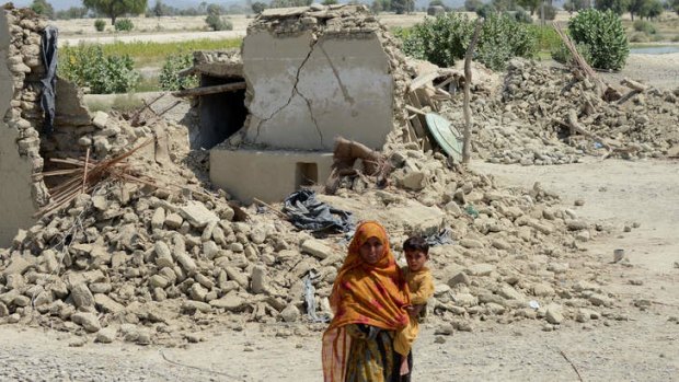 A Pakistani earthquake survivor holds her child in front of collapsed mud houses in Labach, in the earthquake-devastated district of Awaran.