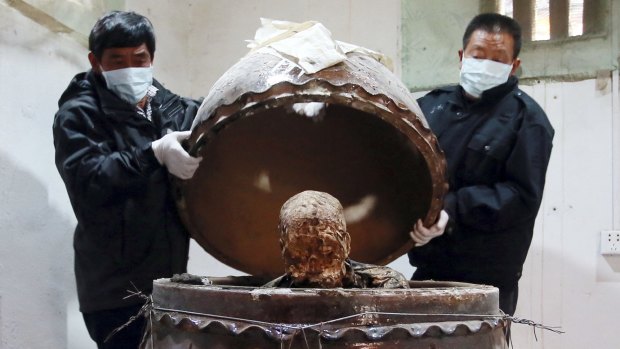 Men open the pot which contains the body of the monk. 