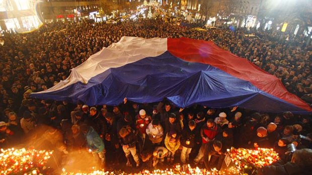 People gather under a Czech national flag as thousands mark the passing of the former Czech president.