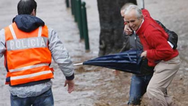 A police officer looks on as a man is helped across a street during floods in downtown Funchal, Madeira.