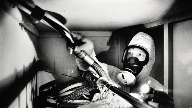 Dmark Giersch with his protective gear on crawls into a cupboard of a house in Campbell to vacuum away dust and asbestos that may have leaked into the house from the roof through cracks at the top of built in robes. From the original removal program.
