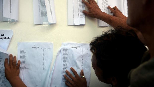 Grim task: People look for names of missing relatives on lists of survivors.