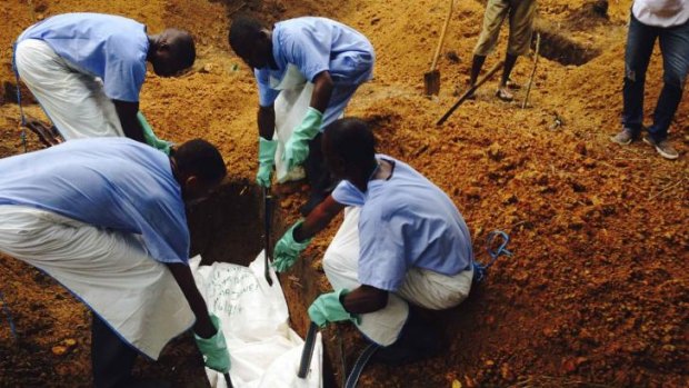 Volunteers lower a corpse, which is prepared with safe burial practices to ensure it does not pose a health risk to others and stop the chain of person-to-person transmission of Ebola, into a grave in Kailahun, Sierra Leone.