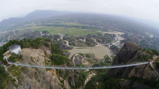Tourists walk on the suspension bridge made of glass at the Shiniuzhai National Geological Park.