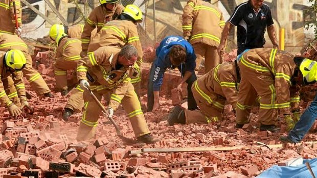 Firemen and workers frantically dig into the fallen brick wall.
