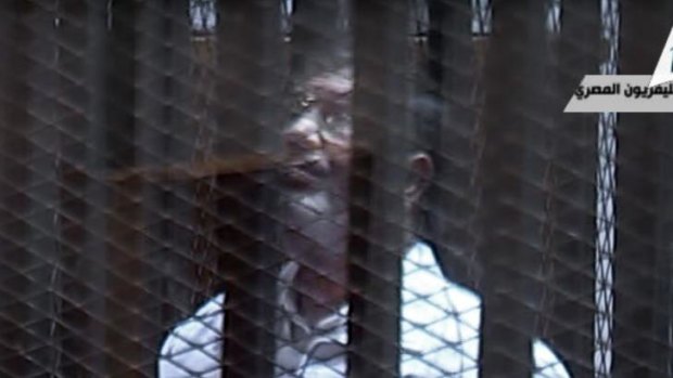 Cone of silence ... toppled President Mohamed Mursi stands inside a glass-encased metal cage  for the start of a new trial Tuesday over charges from prison breaks during the country's 2011 revolution.