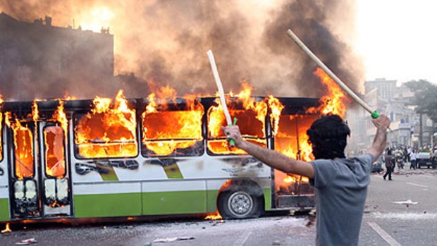 An Iranian protester stands next to a burning bus during clashes with Iranian police at a demonstration in Tehran on June 20.