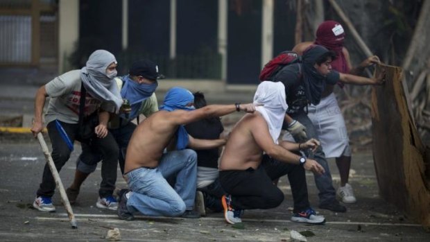 Anti-government protesters take cover during clashes with riot police in Caracas, Venezuela.