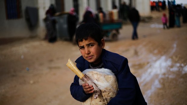A Syrian boy displaced from eastern Aleppo holds a sandwich and bread bag in the village of Jibreen on Saturday.