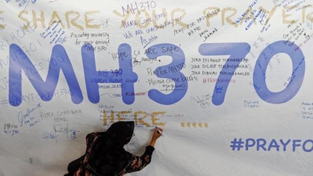 A woman writes a message of support for the passengers of the missing plane on a banner at Kuala Lumpur airport.
