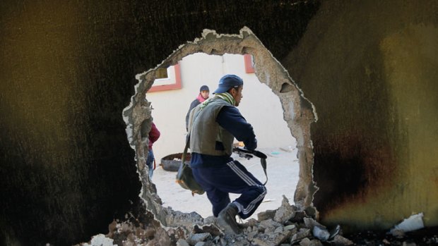 A rebel fighter moves through a hole punched in a wall.
