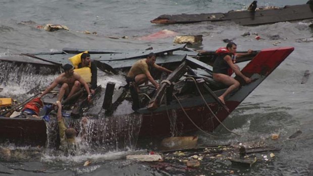 Men cling to the wreckage of a wooden boat in Flying Fish Cove, Christmas Island.