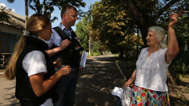 Deputy head of the OSCE mission Alexander Hug (second from right) talks with retired kindergarten teacher Era Pavlovna, 76, (right) after handing her a pamphlet on how to return debris of MH17 crash, in Rassypnoe.