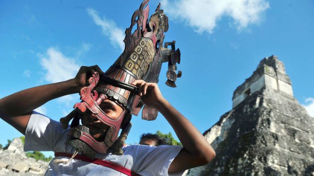 Joining the dots: A man places a Mayan mask on his head in front of a Mayan temple in the city of Tikal.