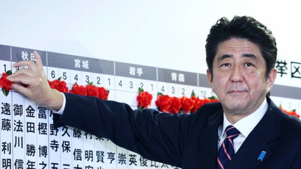 Back with a vengeance ... Japan's former prime minister Shinzo Abe places a paper rose on an LDP candidate's name to indicate an election victory at the party's headquarters in Tokyo on Sunday.