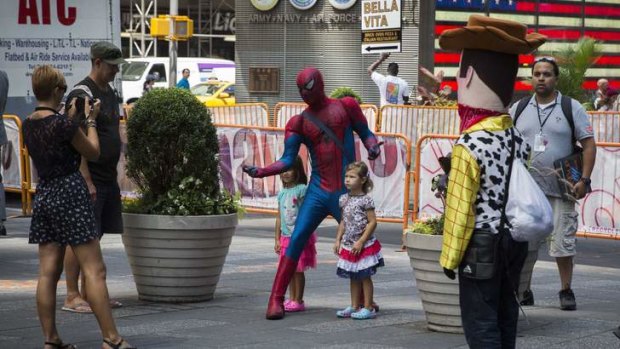 A person dressed in a Spiderman costume stands with children Times Square.