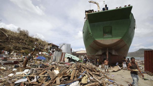 A survivor walks beside a ship that was washed ashore hitting makeshift houses near an oil depot in Tacloban city.