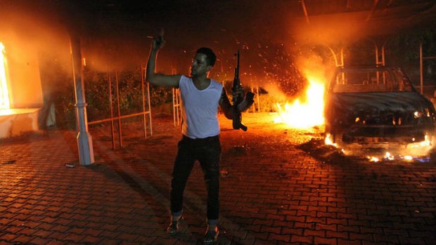 An armed man waves his rifle as buildings and cars are engulfed in flames after being set on fire inside the US consulate compound in Benghazi.