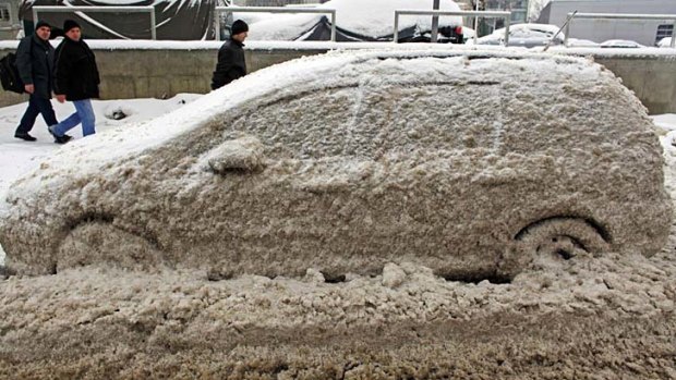 People walk past a car covered in snow and ice in Bucharest.