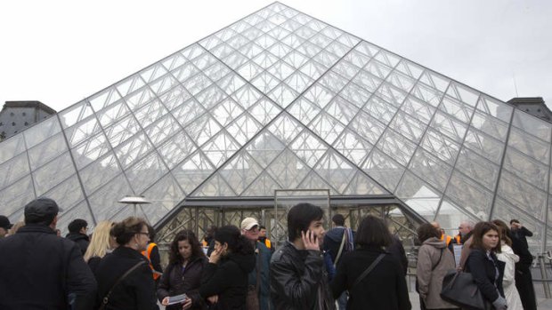 Visitors stands in front of the entrance to the famous Louvre museum in Paris.