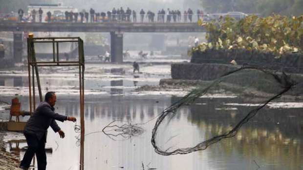 A fisherman casts his net into the muddy waters of a polluted canal in central Beijing.
