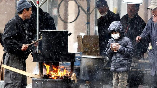 A boy waits for boiled water to make instant noodles outside a shelter for the homeless in Sendai.