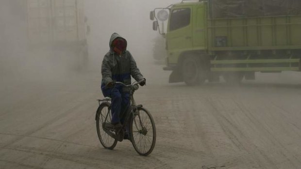 A man covers his face while riding a bicycle on a road covered with ash from Mount Kelud in Solo.