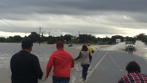 Rescuers rush to a car that is stranded in flood waters in Maitland.