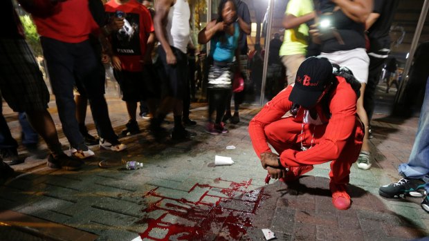 A man squats near a pool of blood after a man was shot during a protest in Charlotte.