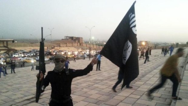 An ISIL militant holds an ISIL flag and weapon in the Iraqi city of Mosul on June 23, 2014.